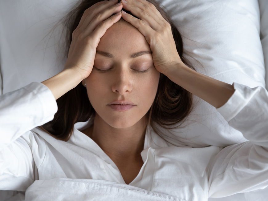 Frau liegt im Bett und hält sich den Kopf