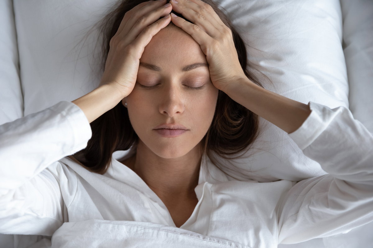 Frau liegt im Bett und hält sich den Kopf