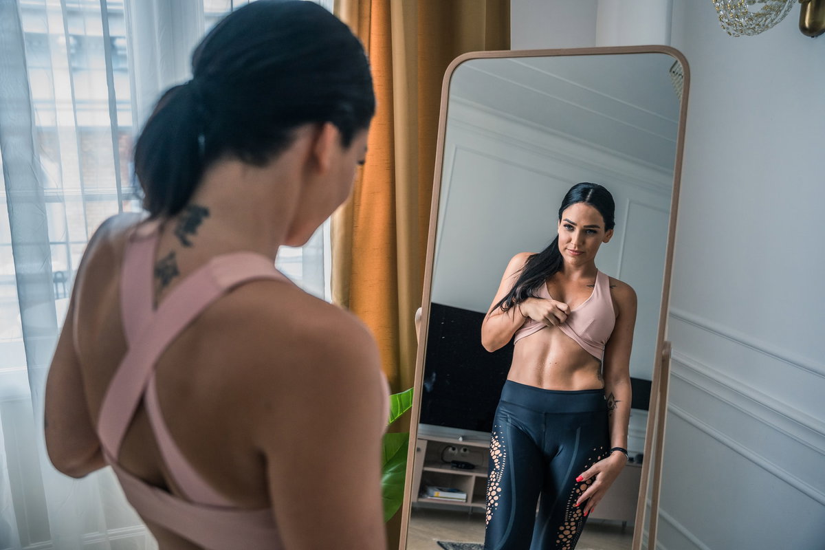 Frau steht vor Spiegel und betrachtet ihren Bauch