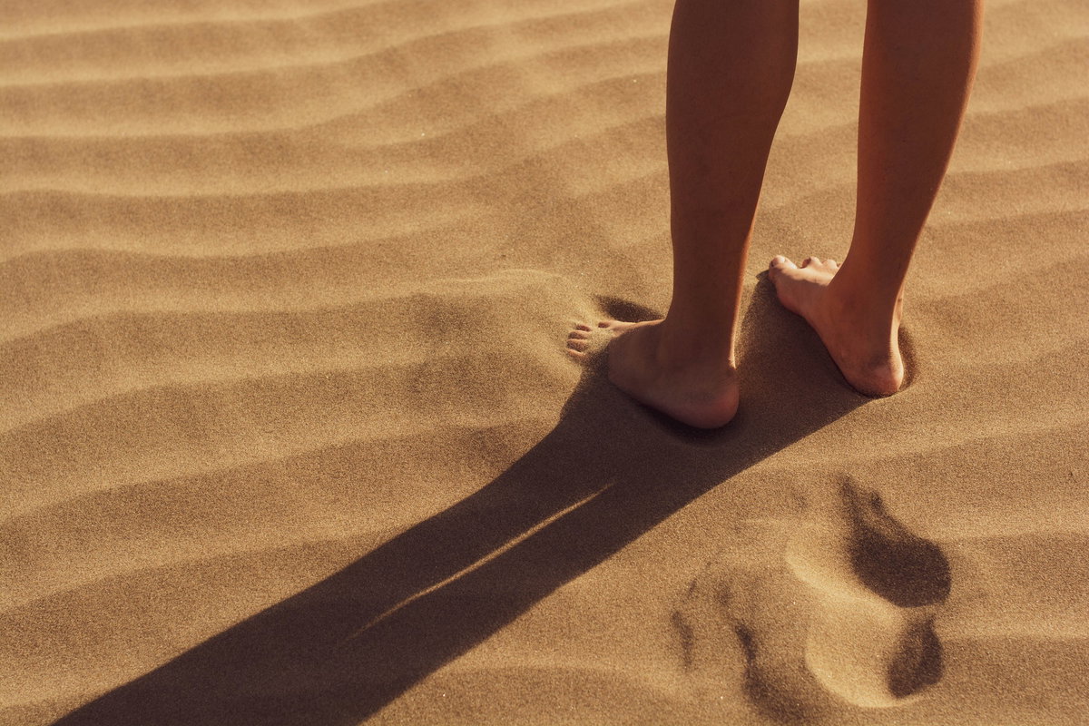 Frau steht barfuß im Sand