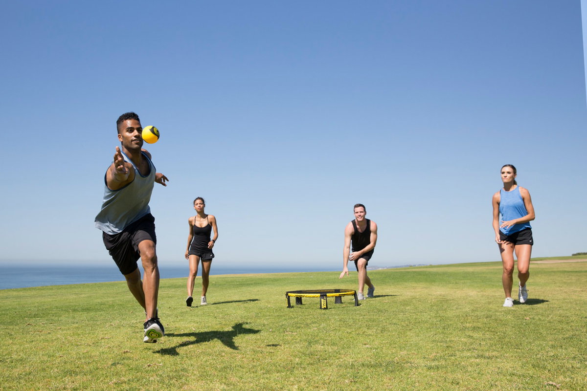 Menschen spielen auf einer Wiese Spikeball