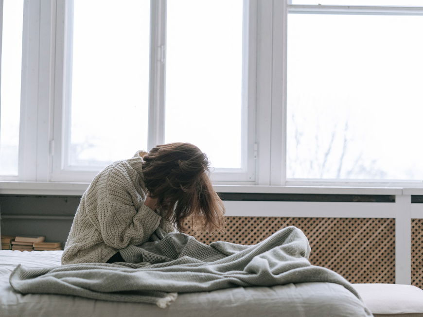 Frau sitzt im Bett und vergräbt ihr Gesicht in ihren Händen