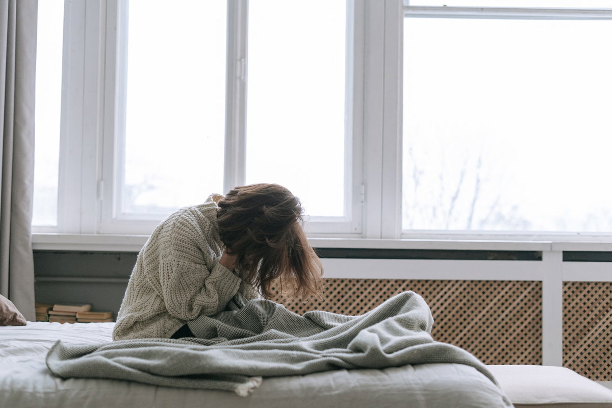 Frau sitzt im Bett und vergräbt ihr Gesicht in ihren Händen