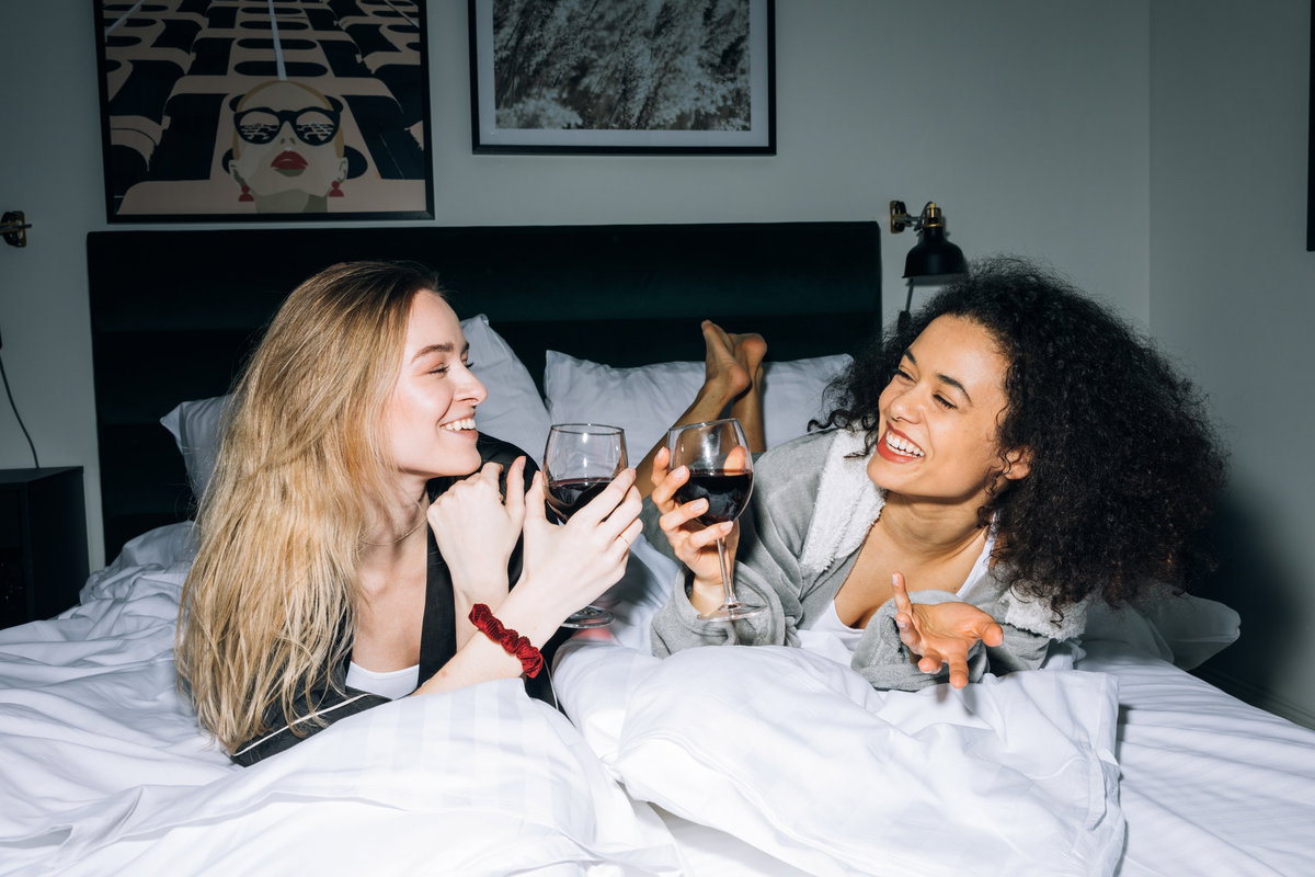 Frauen liegen auf einem Bett und trinken Rotwein