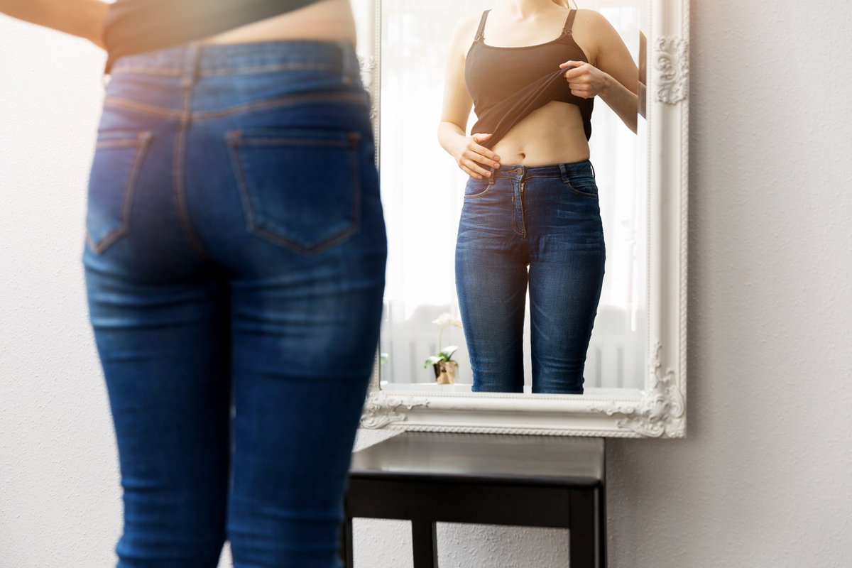 Frau betrachtet ihren Bauch im Spiegel
