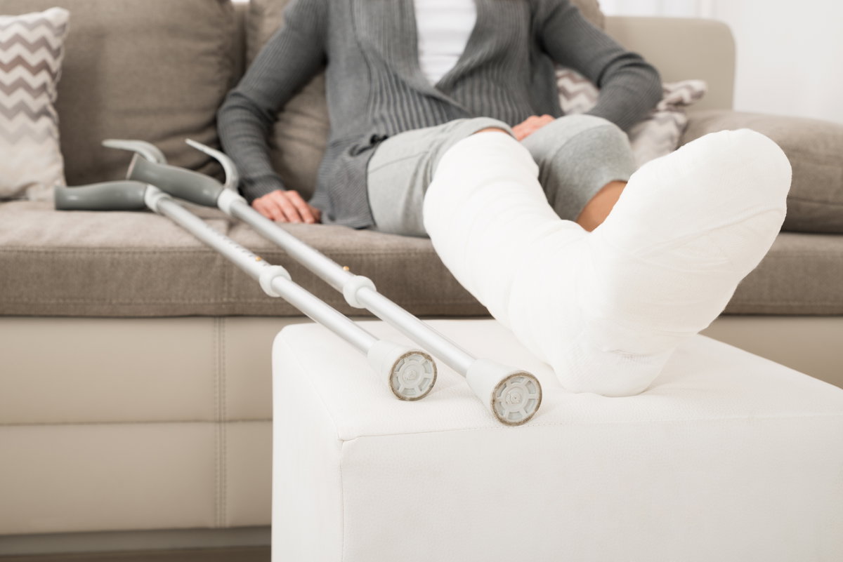 Frau mit Gips und Krücken sitzt auf dem Sofa