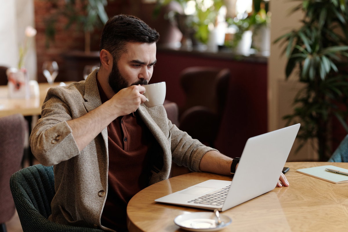 Mann sitzt vor einem Laptop und trinkt Kaffee