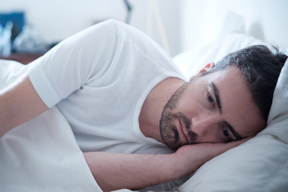 Mann liegt traurig im Bett