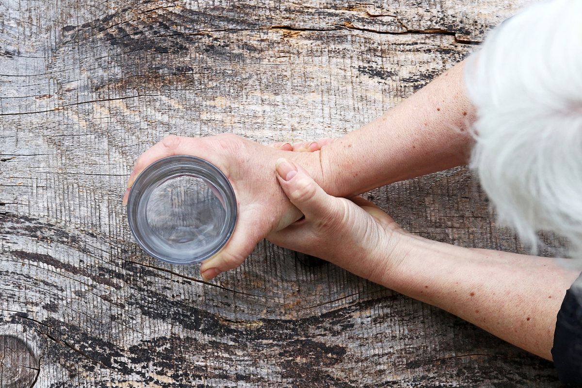 Frau mit grauen Haaren hält Wasserglas in den Händen