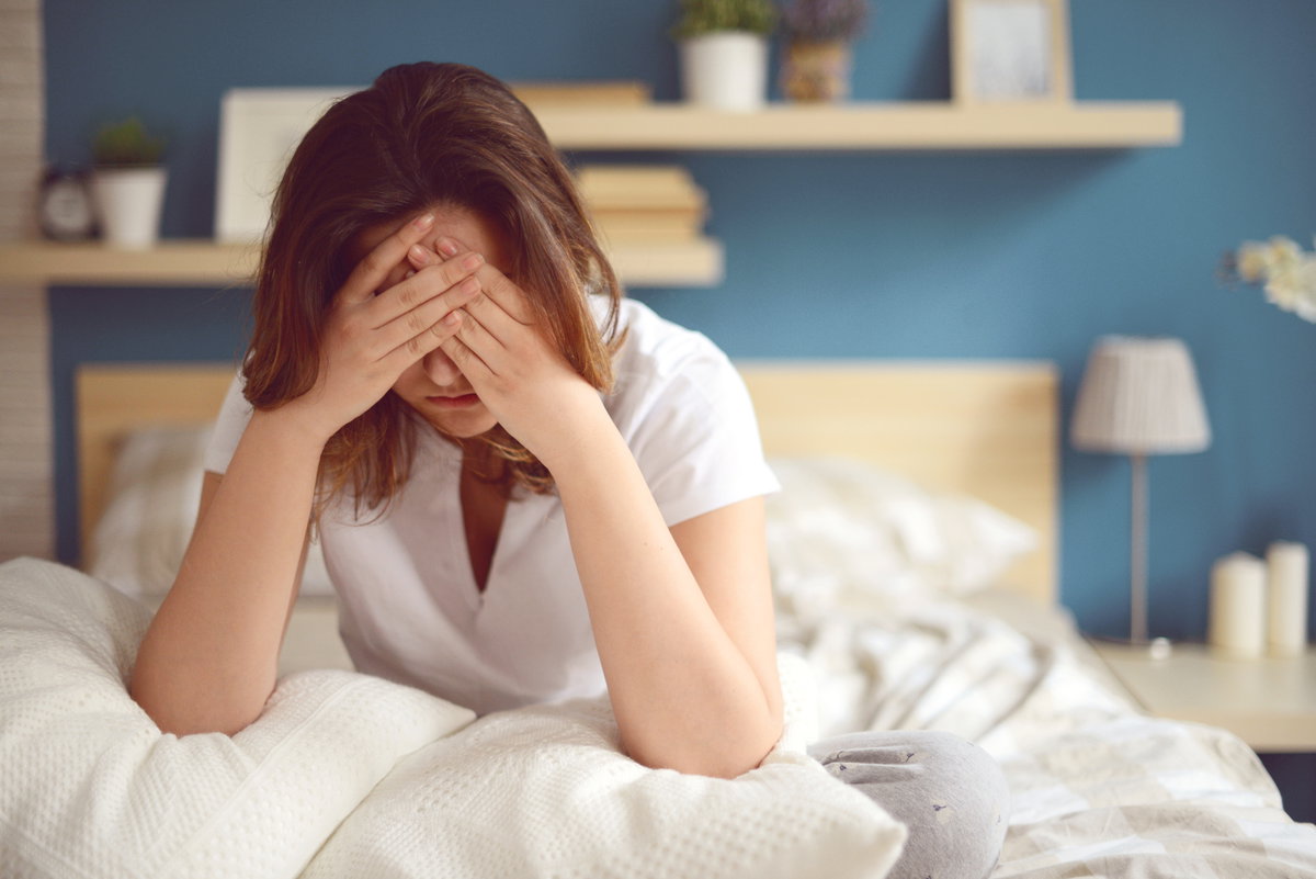 Frau mit Erschöpfung sitzt im Bett mit Händen vor dem Gesicht