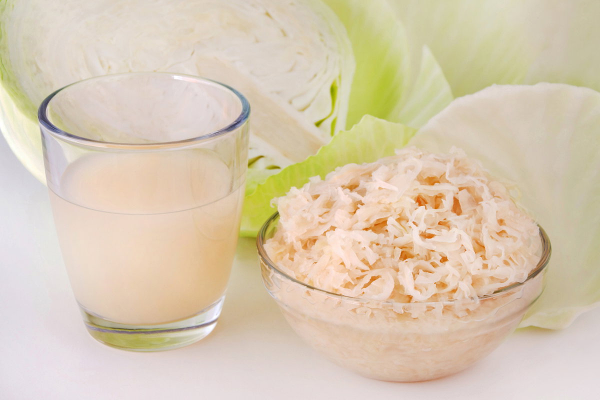 Sauerkraut und Sauerkrautsaft vor aufgeschnittenem Weißkohl