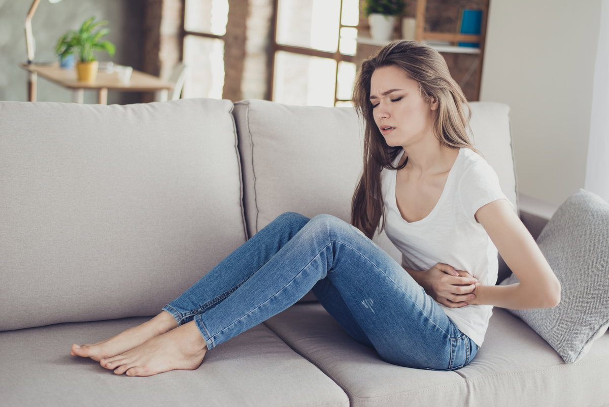 Frau mit Bauchschmerzen sitzt auf Couch