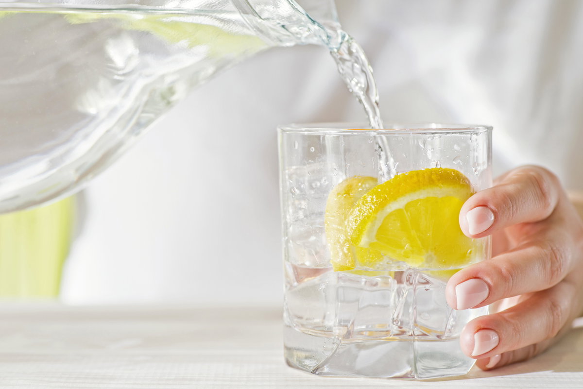 Wasser wird in ein Glas mit Zitrone gegossen