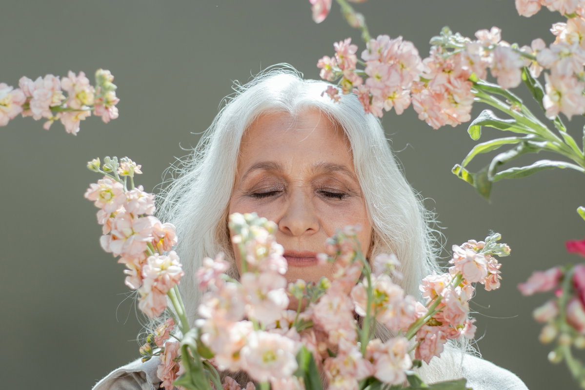Frau mit grauen Haaren riecht an Blumen
