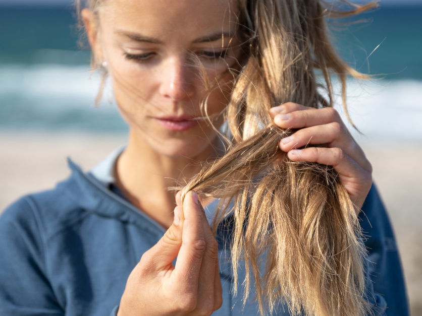 Frau beobachtet Spliss an den eigenen Haaren