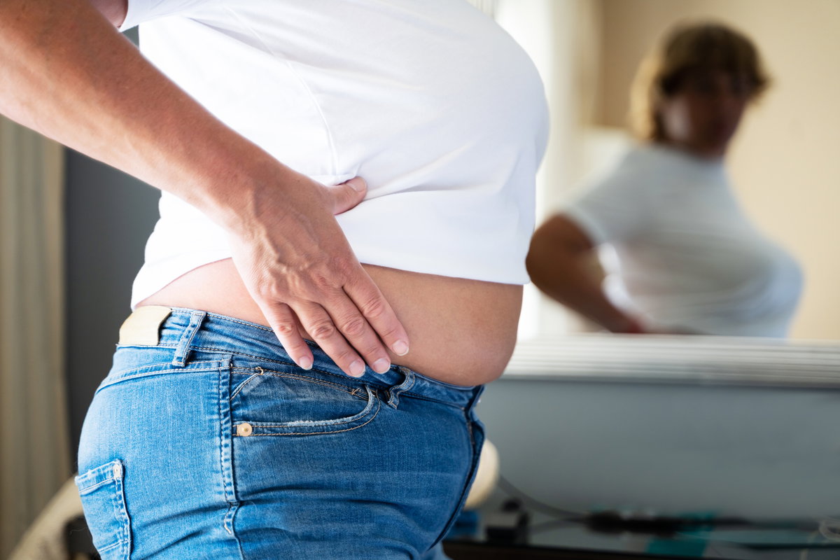 Frau guckt sich ihren Bauch im Spiegel an