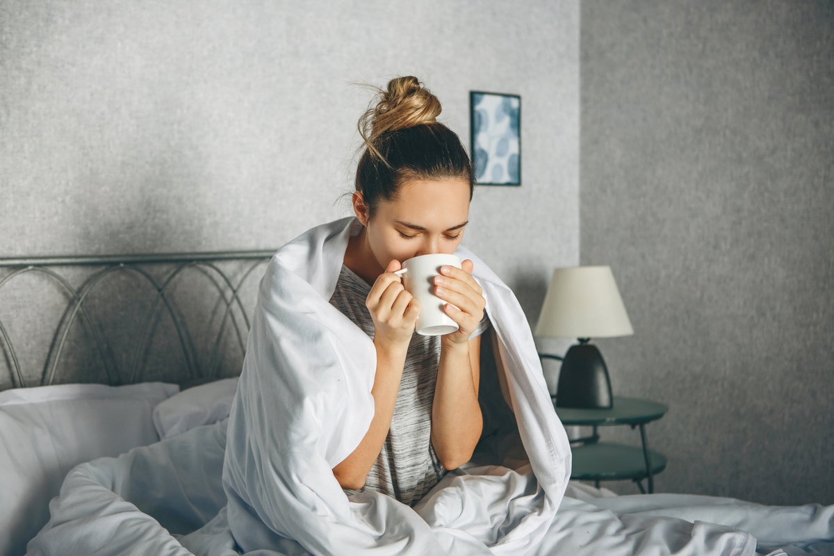 Kranke Frau trinkt Tee im Bett