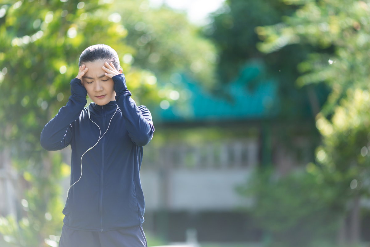 Joggerin mit Erkältung fasst sich an schmerzenden Kopf