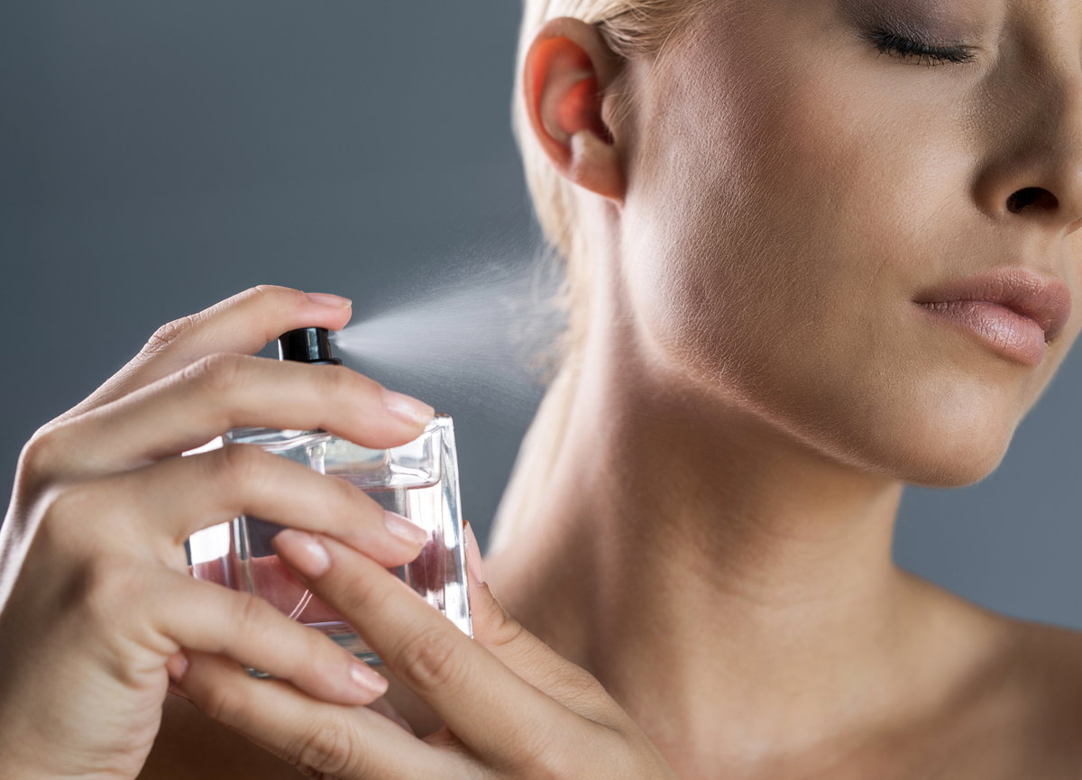 Frau sprüht Parfum auf ihren Hals