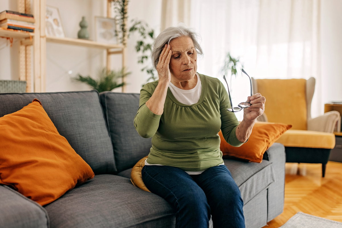 Alte Frau auf der Couch fasst sich wegen Schwindel an den Kopf