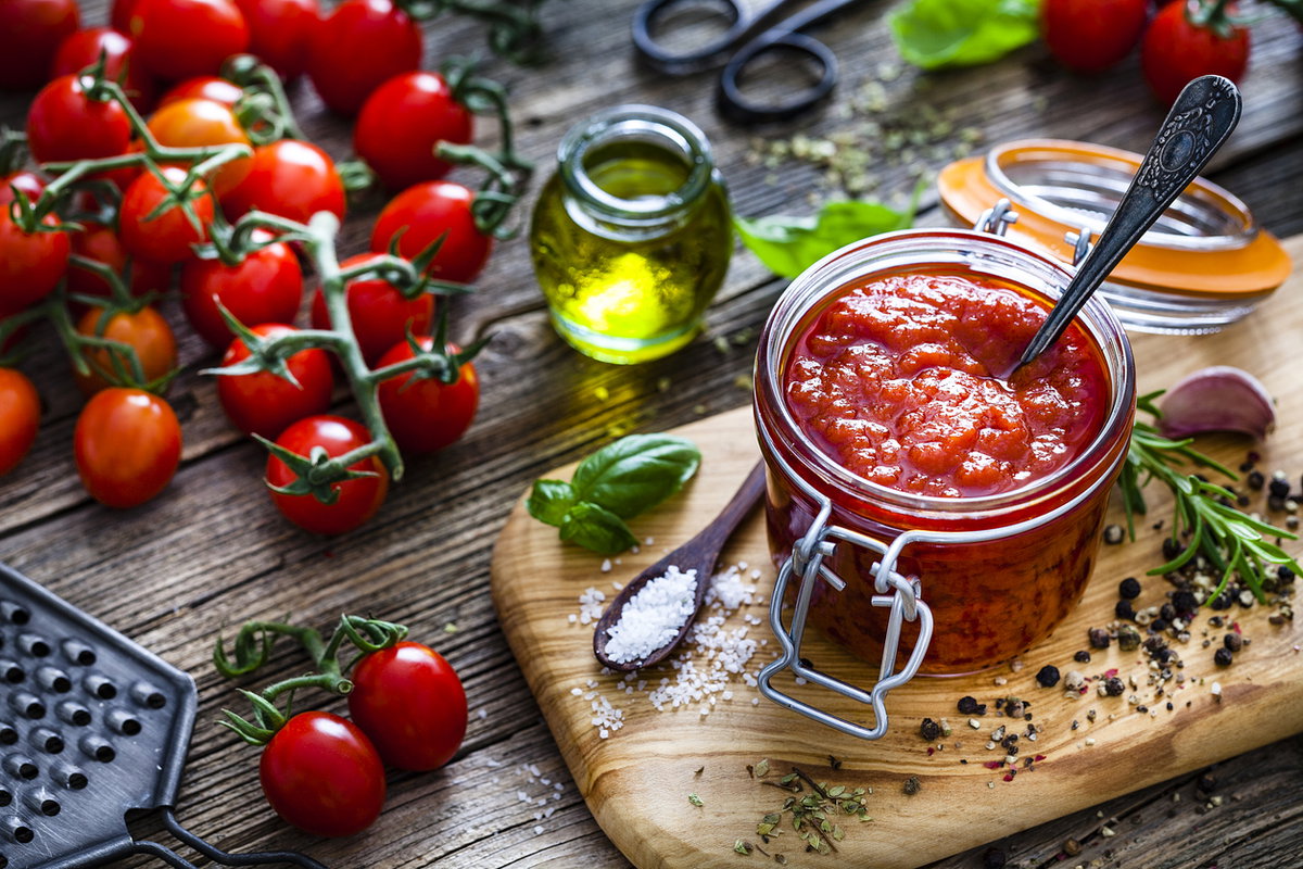 Hausgemachte Tomatensoße in Glas mit frischen Zutaten auf Brett