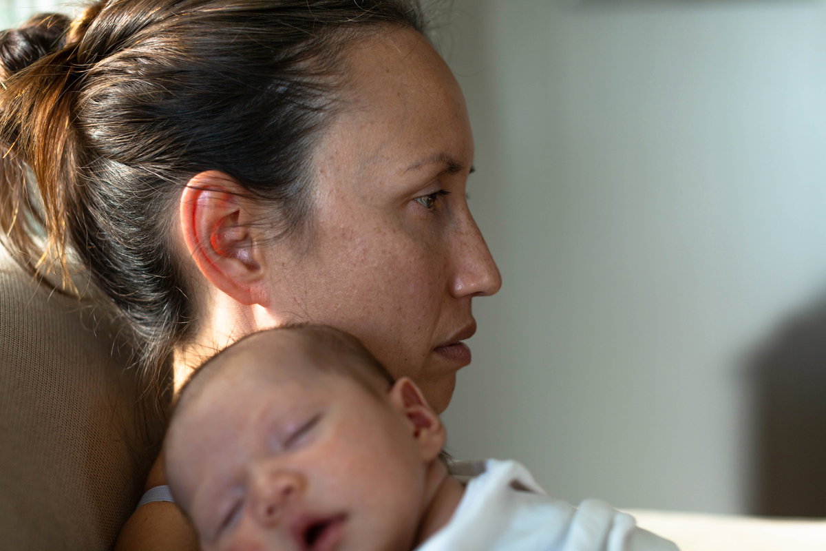 Frau mit Wochenbettdepression und Baby auf dem Arm starrt ins Leere