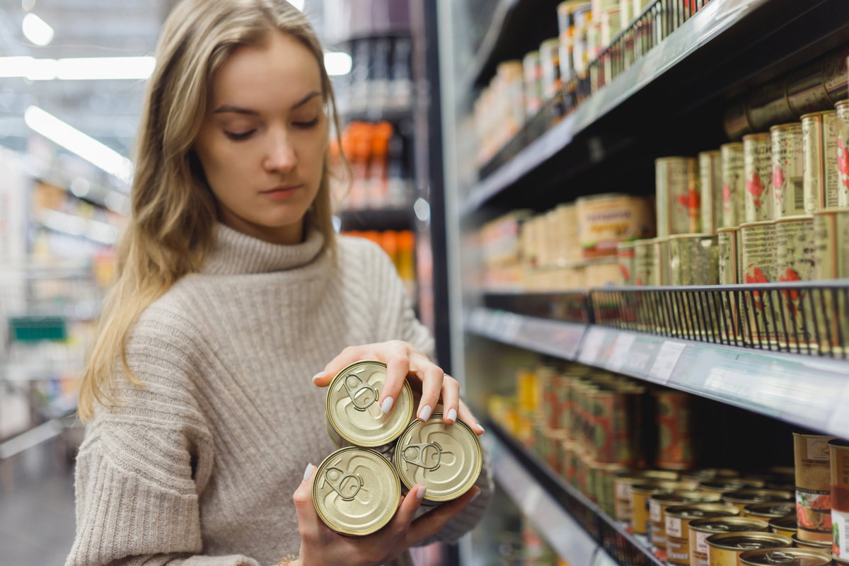 Frau nimmt Konserven aus Supermarktregal