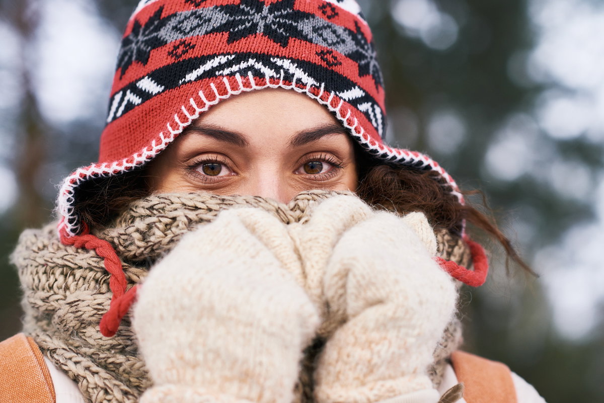 Frau mit Schlappmütze wärmt Nase im Winter unter dickem Schal