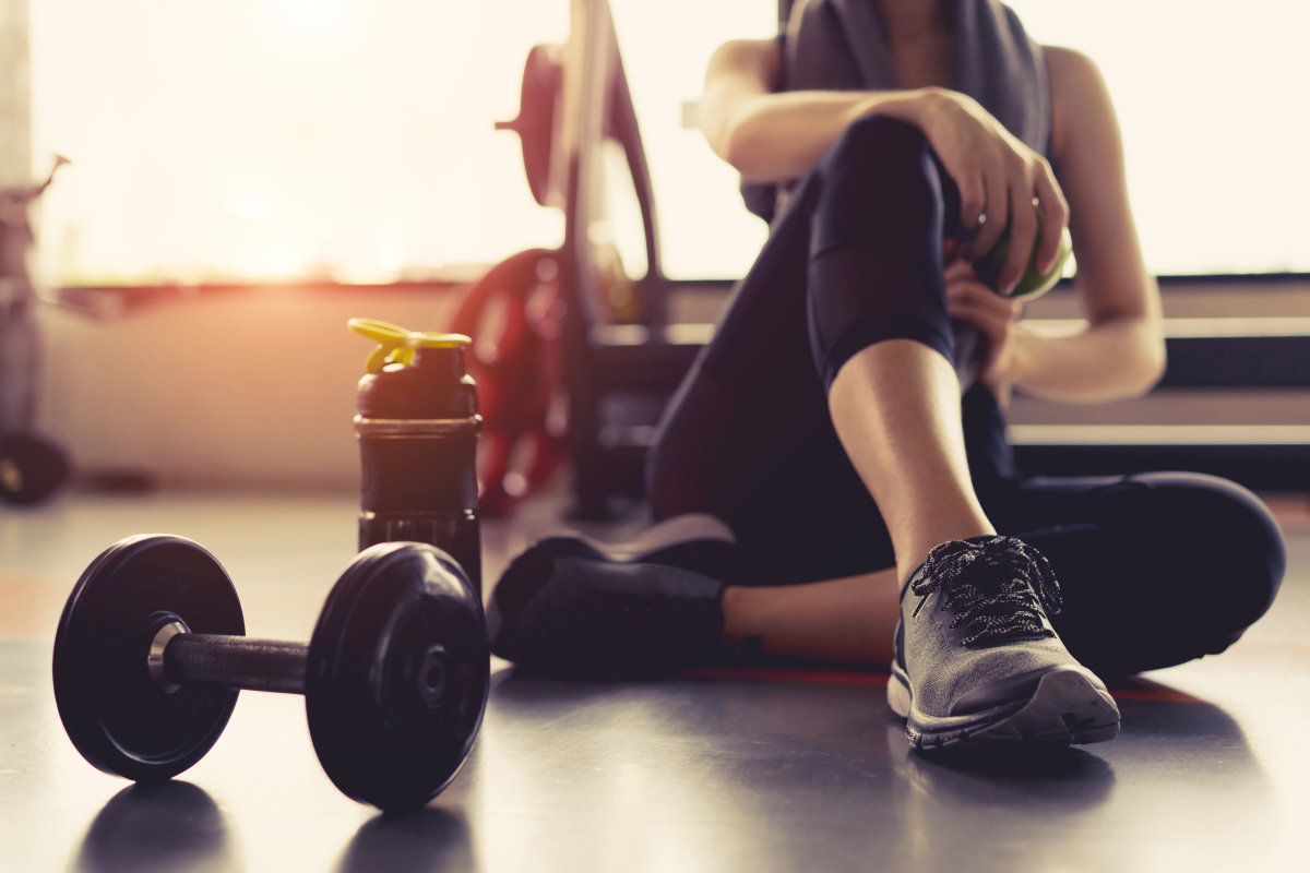 Frau sitzt erschöpft im Fitnessstudio