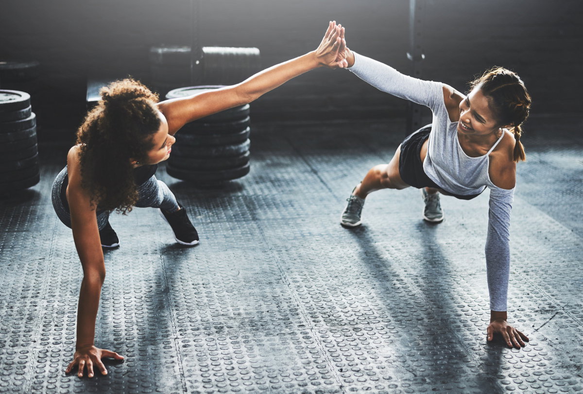 zwei Fitnessfreundinnen machen Plank zusammen und klatschen ab