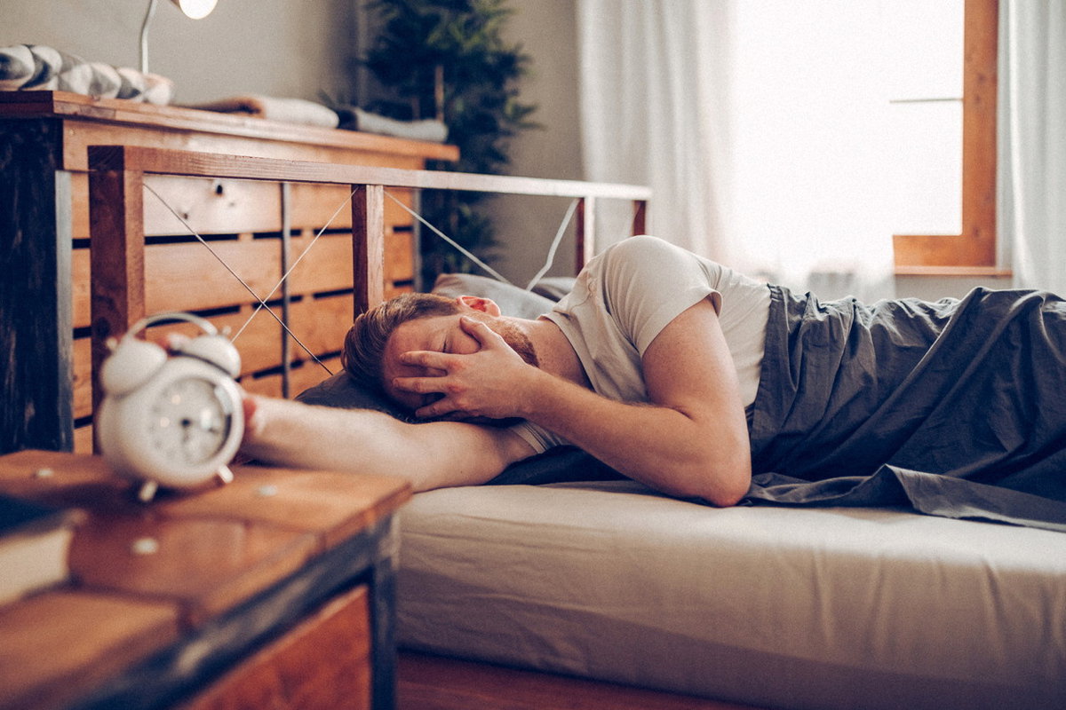 Müder Mann hat Schwierigkeiten morgens aus dem Bett zu kommen
