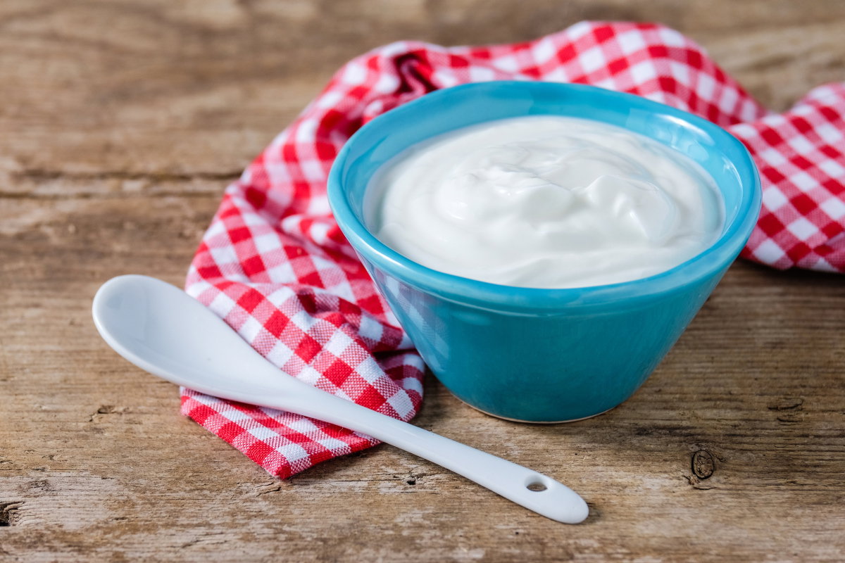 Joghurt in Schüssel auf kariertem Tuch auf Tisch