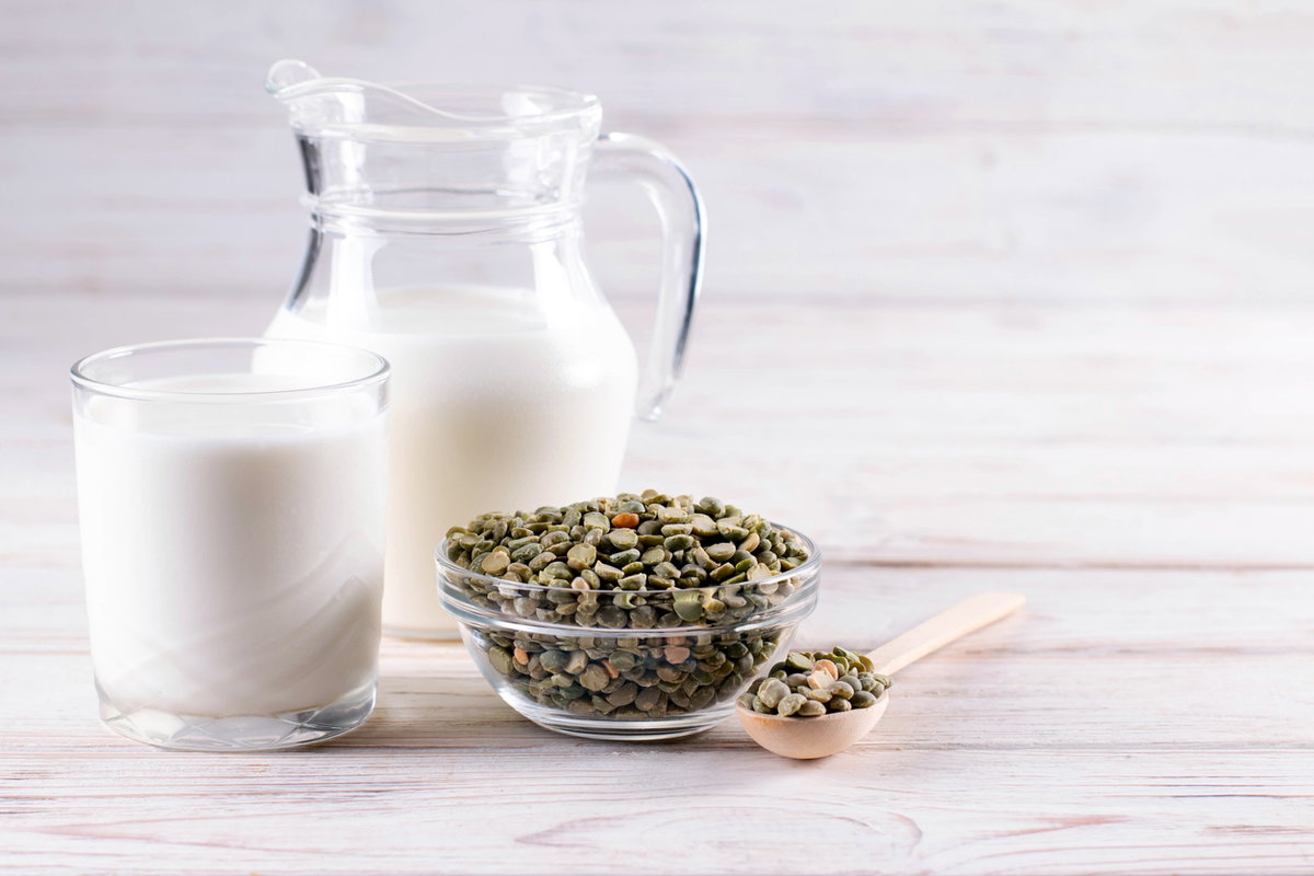 Milchglas und Karaffe mit trocknen, grünen Erbsen davor
