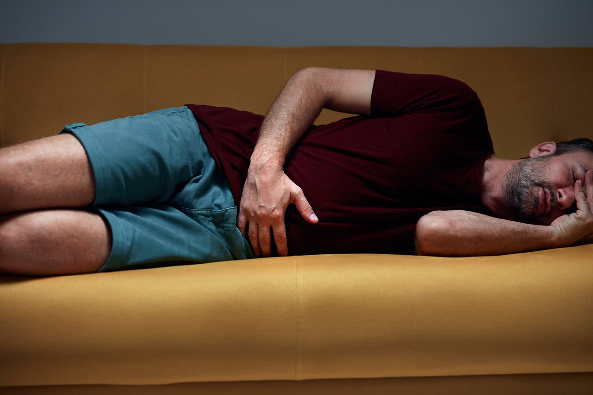 Mann mit Bauchschmerzen liegt auf gelber Couch