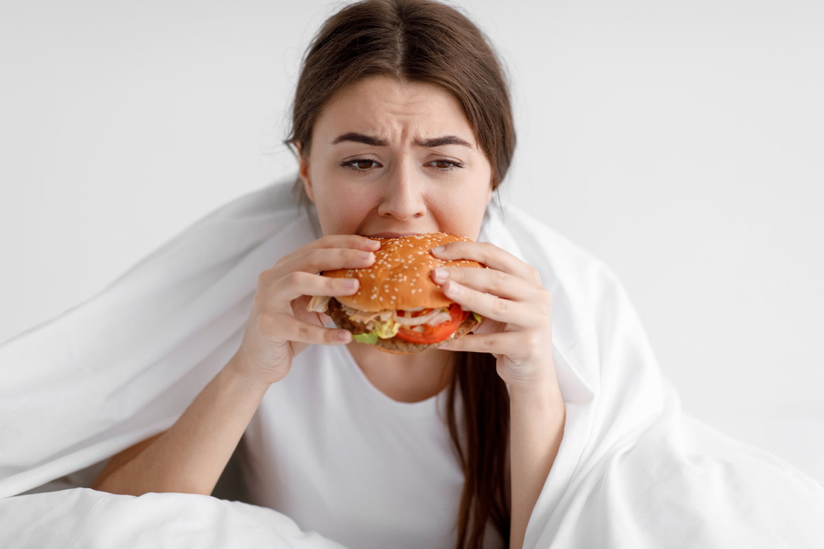 Frau isst im Bett einen Burger