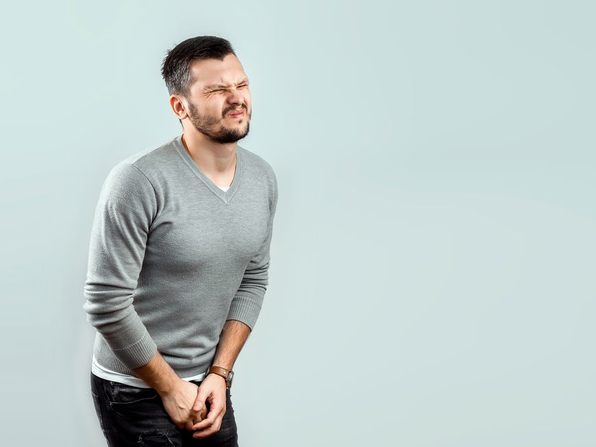 Mann fasst sich mit schmerzverzerrtem Gesicht zwischen die Beine