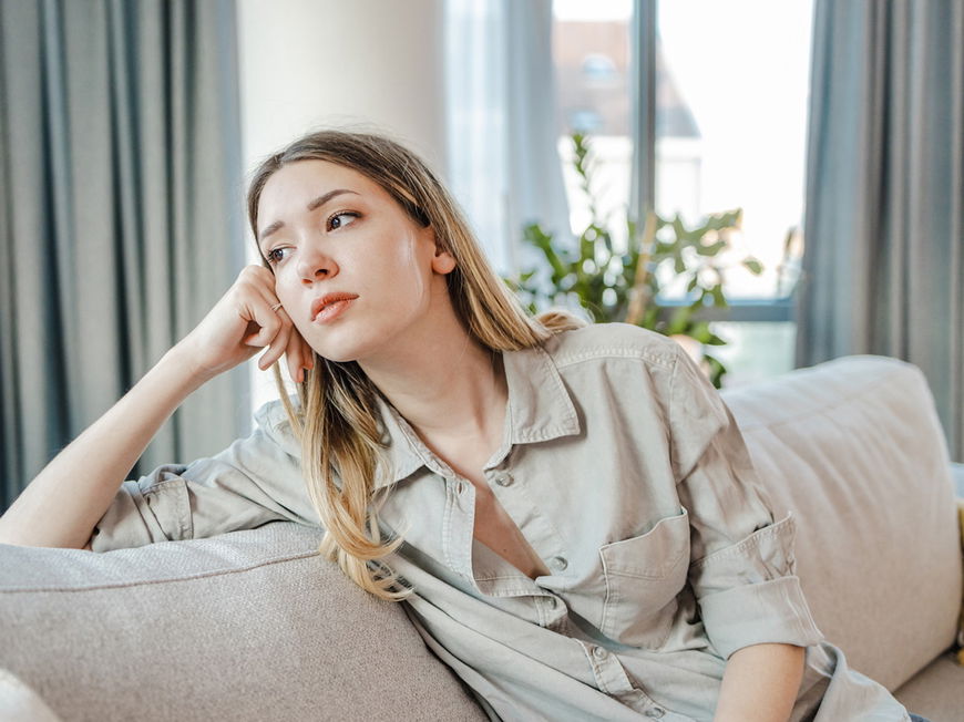 Frau sitzt auf Sofa und guckt traurig