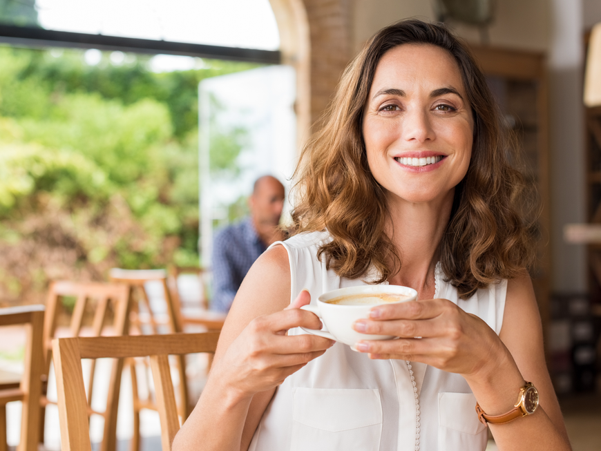 Frau trinkt lächelnd eine Tasse Kaffee