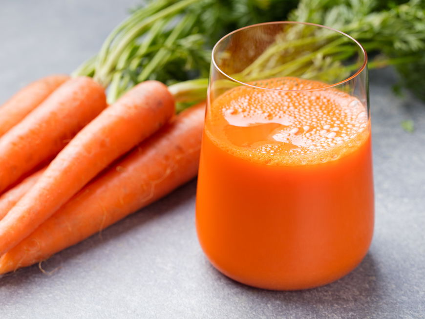 Ein Glas frisch gepresster Karottensaft mit einem Bündel Karotten daneben