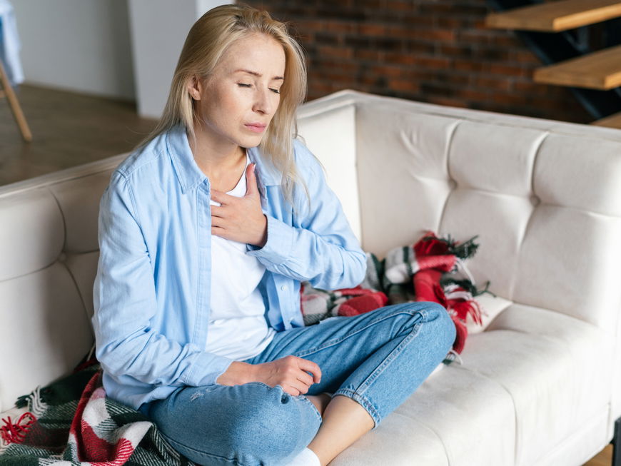 Frau sitz auf Sofa und fasst sich an die Brust