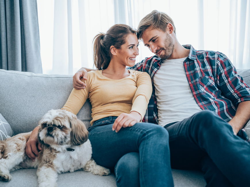 Ein glückliches Paar sitzt zusammen mit ihrem Hund auf der Couch