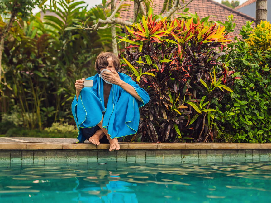 Mann sitzt im Urlaub mit Erkältung am Pool