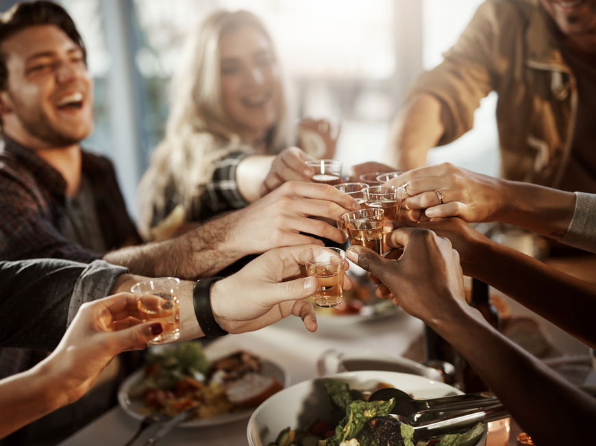 Gemischte Gruppe aus Freunden stößt mit kleinen Schnäpsen beim Essen an