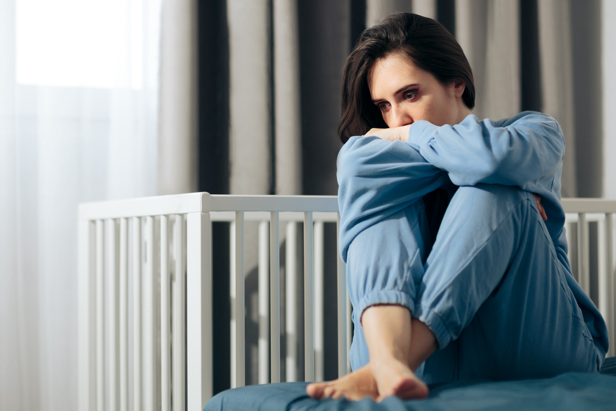 Eine traurige Frau sitzt vor einem leeren Kinderbettchen