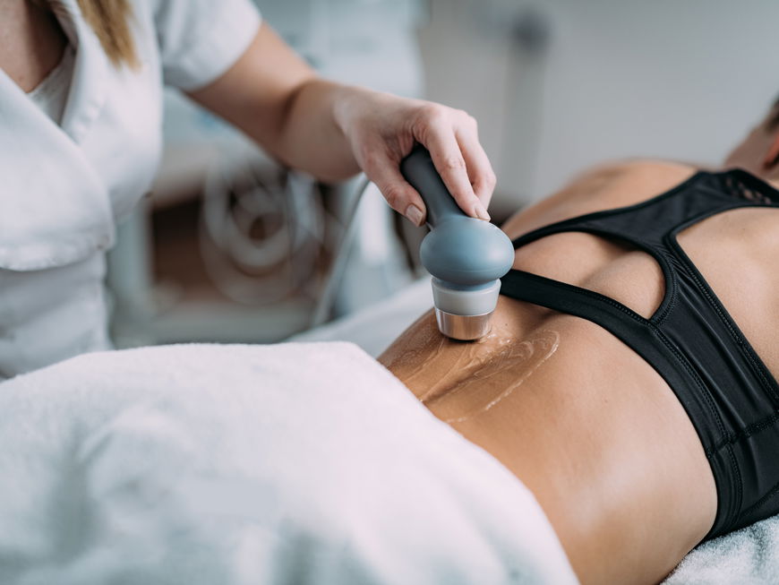 Physiotherapeutin behandelt den Rücken einer Patientin mit einem Ultraschallgerät.