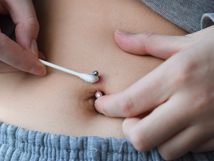 Frau pflegt ihr Bauchnabel-Piercing