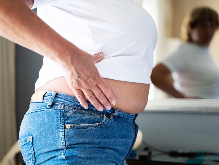 Frau guckt sich ihren Bauch im Spiegel an