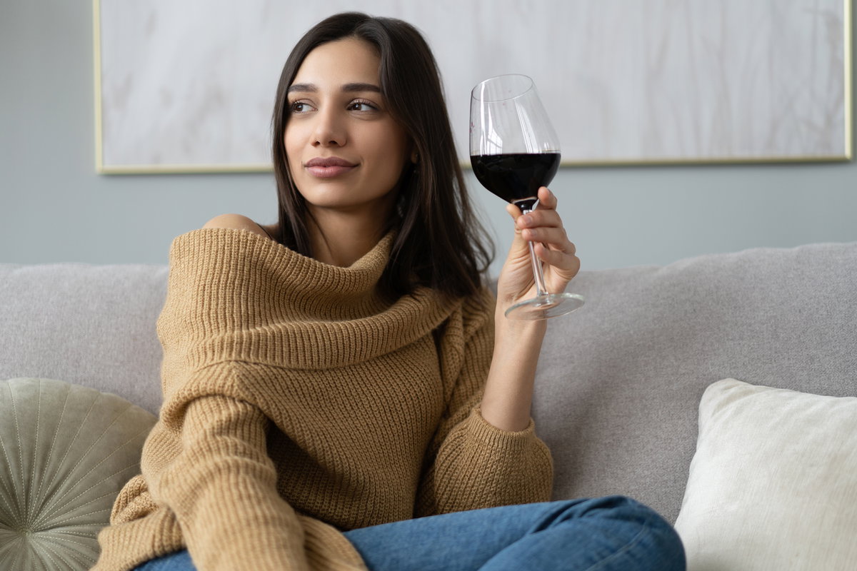 Frau sitzt mit einem Glas Rotwein auf dem Sofa