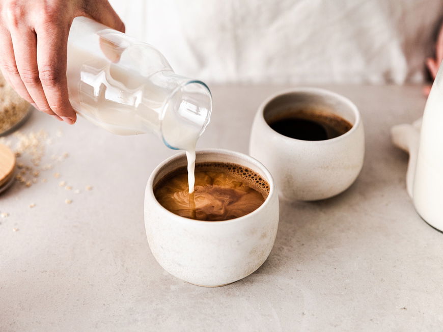 Frau gibt Milch in Kaffee