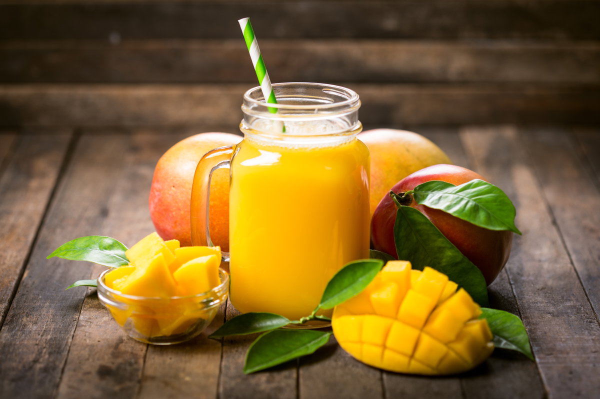 Ein Glas Mangosaft umgeben von Mangofrüchten.